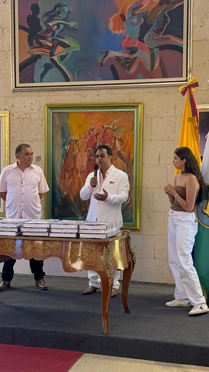 Dr Alrashid speaking into a microphone at the event, with paintings displayed behind him